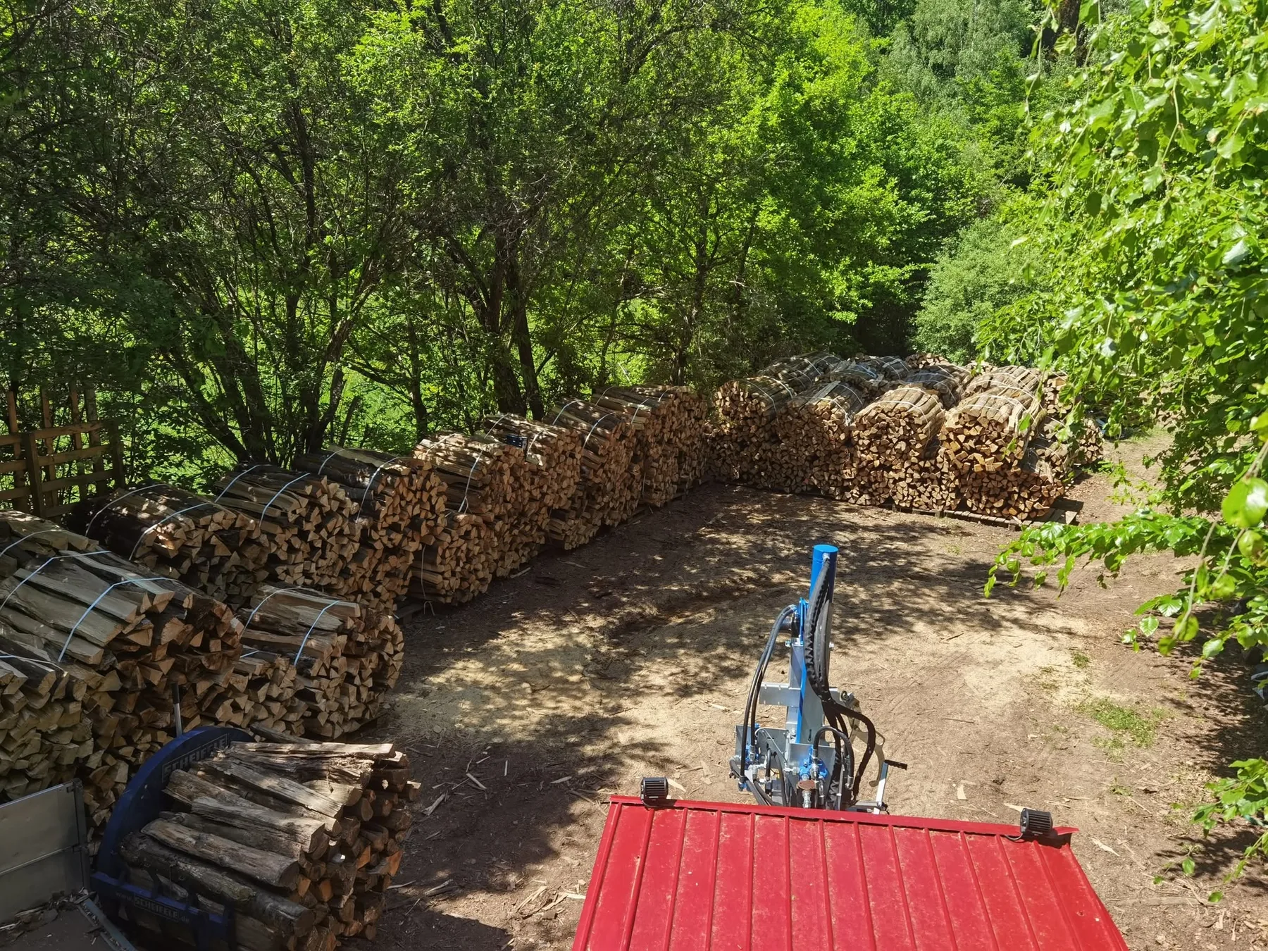 Der Lagerplatz von Brennholz F&M am Waldweg: Reihen gebündelten Brennholzes, Spalter und Anhänger